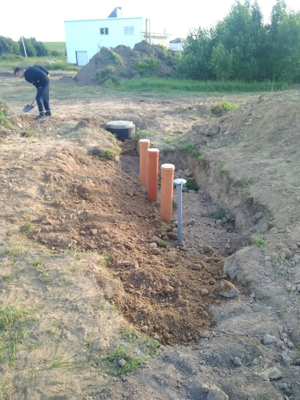 Прокладка канализационных труб в траншее возле строящегося дома.