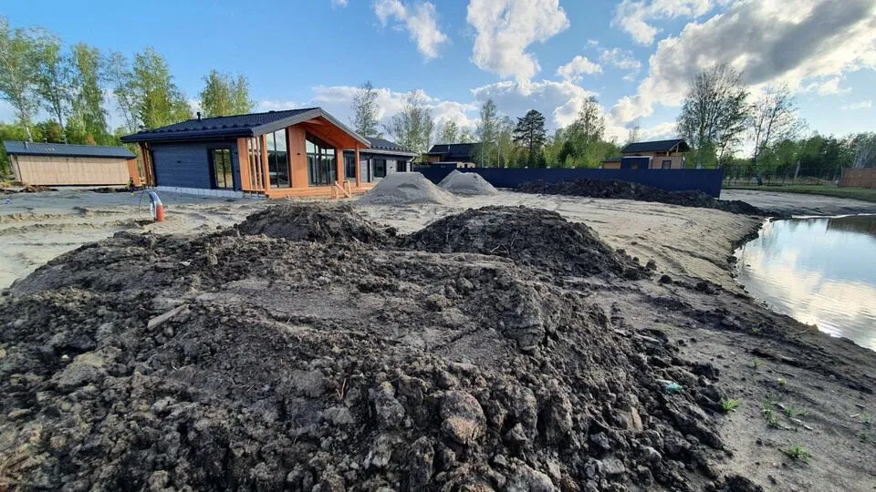Строящийся загородный дом, земляные насыпи и небольшой пруд.