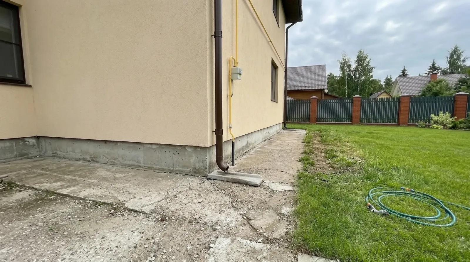Бежевый дом с газовой трубой и зелёным двором.