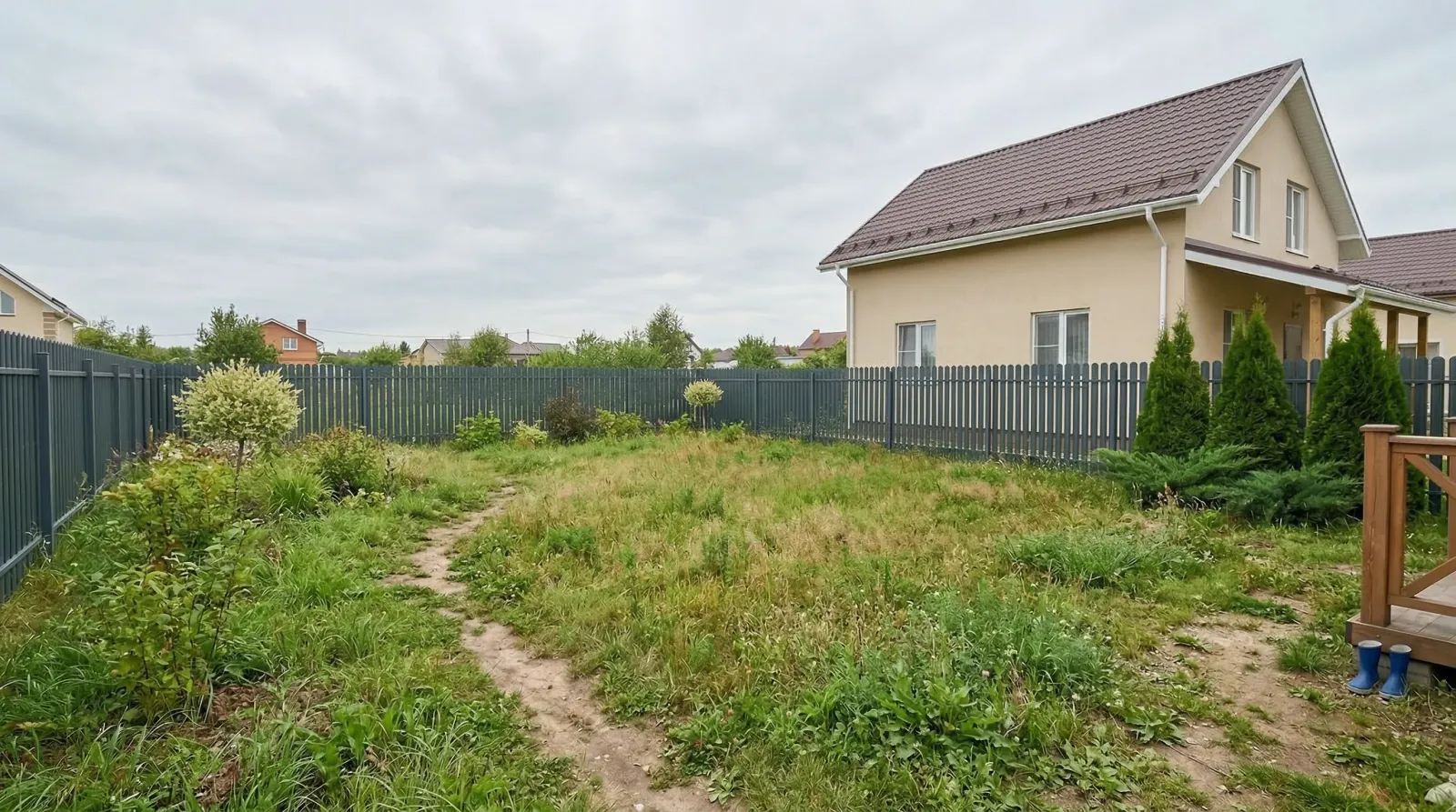 Заросший травой участок рядом с загородным домом.