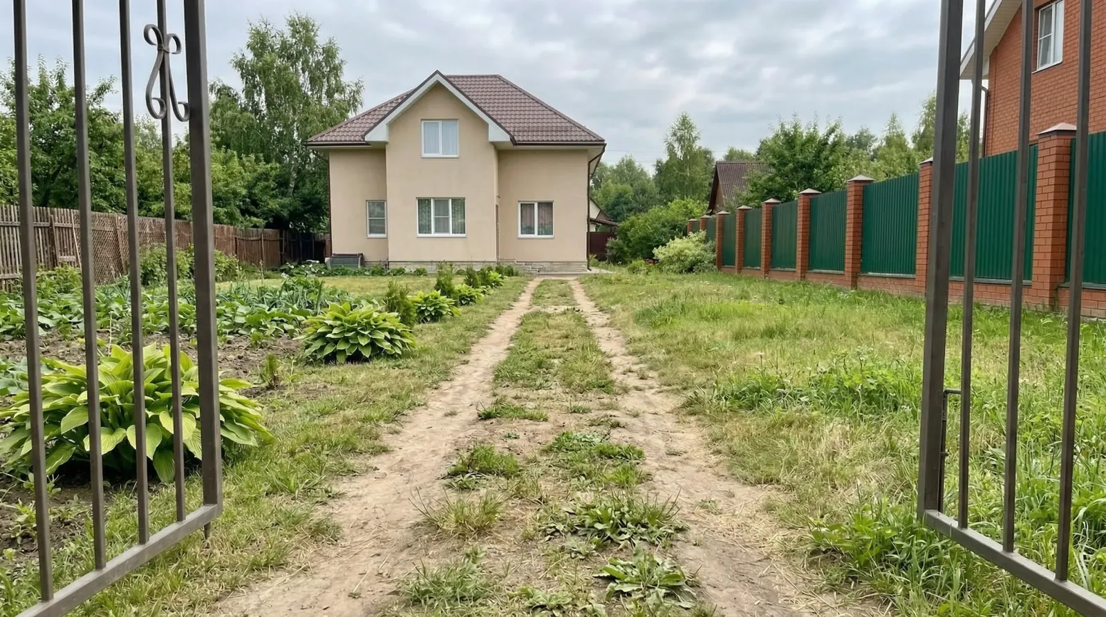 Загородный дом за открытыми воротами и зелёным участком.
