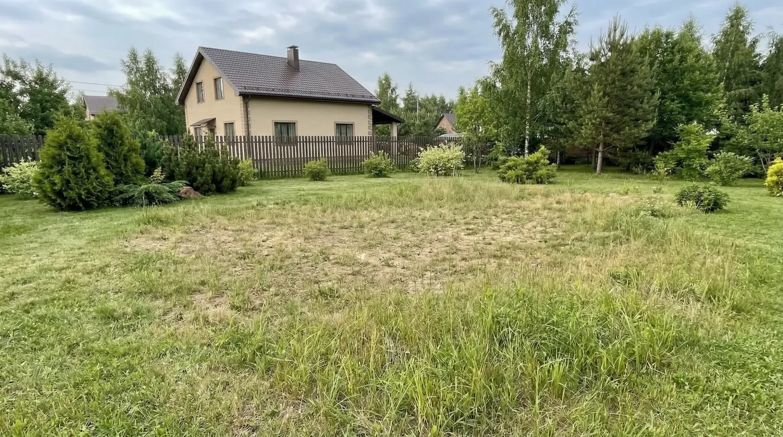 Загородный дом с огороженным зелёным участком и деревьями.