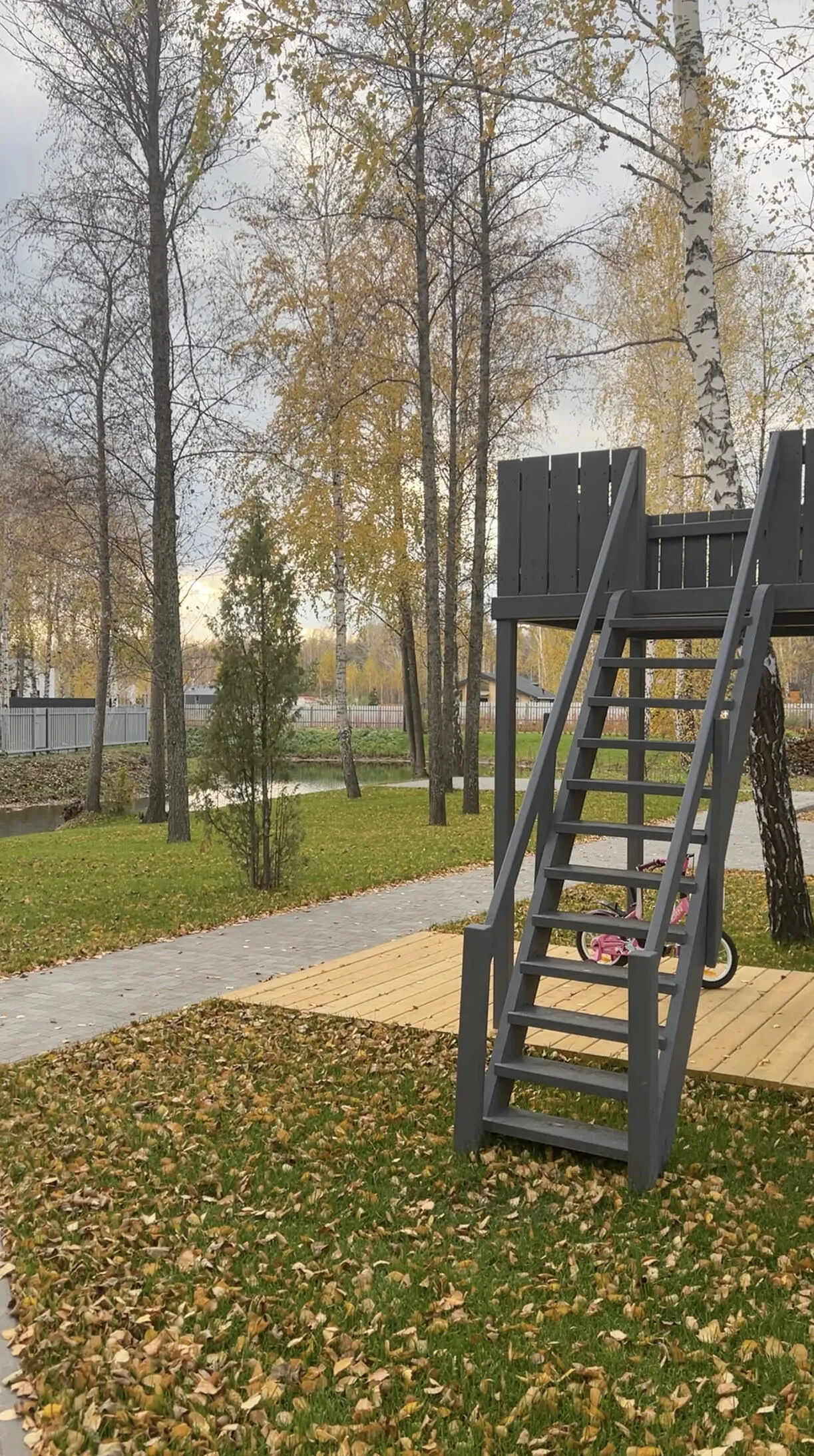 Высокая деревянная горка среди осенних берёз в парке.