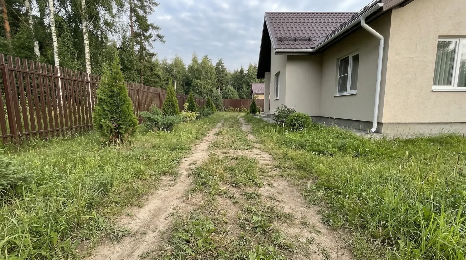 Загородный дом, заросший двор и грунтовая дорожка вдоль забора.