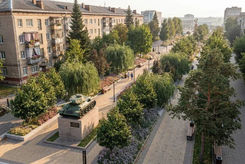 Зелёный городской бульвар с танком-памятником среди жилых домов.